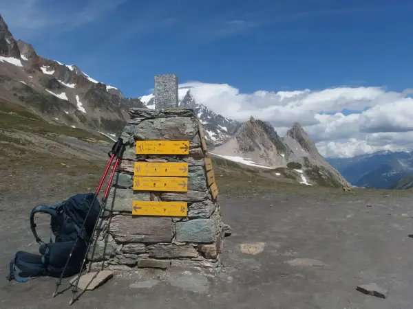 Wegweiser für die Tour du Mont Blanc Etappen: Rucksack und Stöcke liegen bereit. Bergpanorama mit blauen Himmel und Wolken.