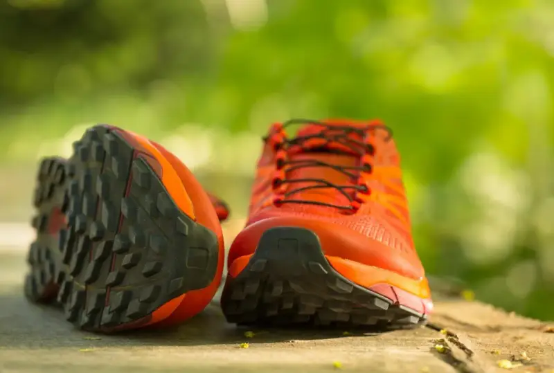 Leuchtend orange Trailrunning-Schuhe mit grobstolliger Sohle, bereit für neue Abenteuer. Perfekt, um bergschuhe neu besohlen zu lassen und wieder loszulegen.